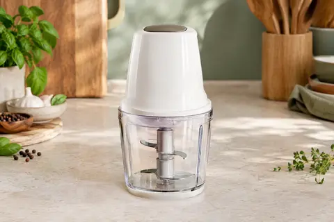 Hachoir électrique compact blanc avec bol et quatre lames inox posé sur un plan de travail clair
