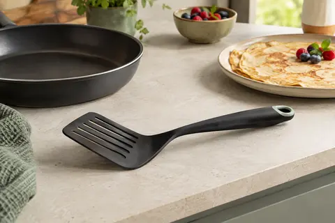 Spatule coudée noire Tefal Ingenio à tête fendue posée sur un plan de travail clair