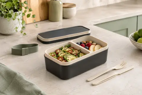 Lunch box bento rectangulaire onyx et beige avec sangle, couverts et deux compartiments sur un plan de travail clair.